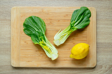 Cut green pak choi cabbage leaves and fresh lemon on wooden board. Fresh Chinese cabbage pak choi in the process of cooking. Top view.