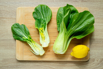 Cut green pak choi cabbage leaves and fresh lemon on wooden board. Fresh Chinese cabbage pak choi in the process of cooking. Top view.