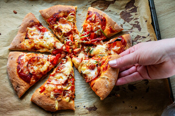 Female hand taking a slice of cut homemade pizza on baking paper. Top view