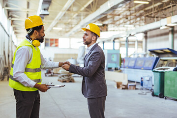 Engineer and Businessman Shaking Hands Inside a Factory Setting