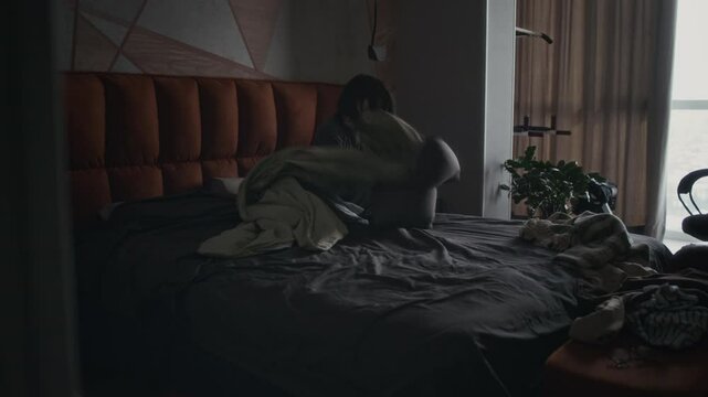 Wide shot of teenage Caucasian girl sitting in unkempt bedroom, contemplating heartbreak or betrayal, then screaming in rage, thumping on pillow, then hiding under duvet and weeping in anguish