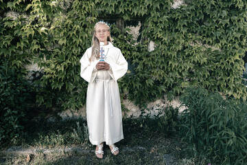 Blonde girl stands in nature for her First Communion in white dress and veil
