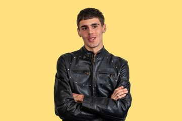 Fototapeta premium Young man wearing black leather jacket with crossed arms on yellow background