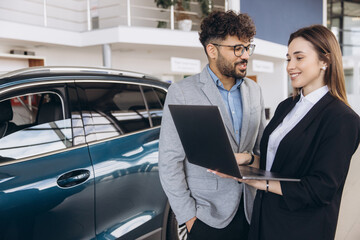 Saleswoman showing information on laptop to customer buying new car