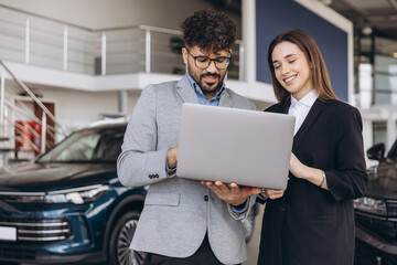 Car salesman showing laptop to customer in a dealership