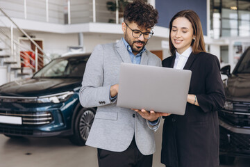 Car dealer showing laptop to customer in a showroom