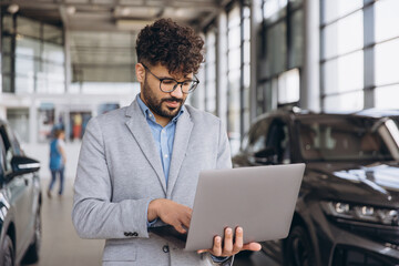 Car salesman working on laptop in car dealership