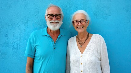 A happy older couple poses against a blue wall.