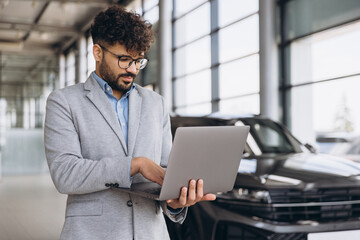 Car salesman using laptop in car dealership showroom