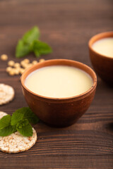 Organic non dairy banana and soy milk in clay cup on brown wooden, side view, selective focus.