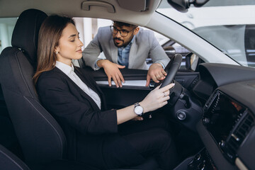 Car salesman showing new vehicle features to businesswoman in dealership