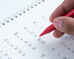 Hand marking date on calendar with red pen – planning, scheduling, and time management concept...