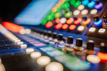 Colorful close-up of a professional audio mixer console with knobs, buttons, and illuminated...