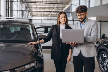 Car salesman showing features on laptop to customer in dealership