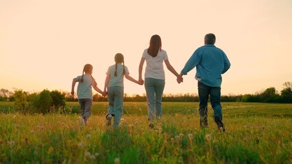 Fototapeta premium Parents kids running holding hands in meadow. Family team walk travel in nature park. Happy family with children walking in nature. Concept of family recreation in nature. Happy family children field