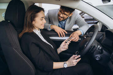 Car salesman giving car keys to businesswoman in a dealership