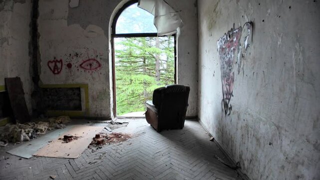 Derelict room in Sanatorium Medea in Tskaltubo, Georgia. Featuring graffiti, a broken floor, and an armchair by a large window, framing a view of lush greenery reclaiming the space