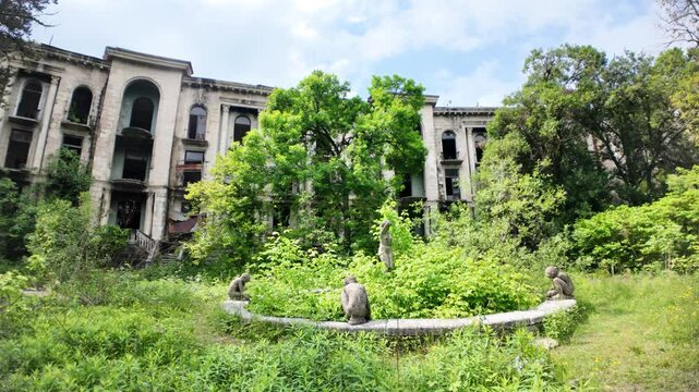 Overgrown vegetation and decaying statues surround the abandoned Sanatorium Medea, a former Soviet-era spa in Tskaltubo, Georgia, showcasing the impact of time and neglect after the USSR's collapse