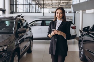 Saleswoman using smartphone at car dealership showroom