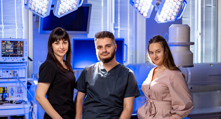 Medical team poses in an operating room. Three healthcare professionals stand confidently in a...