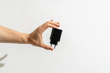 Hand holding a black phone charger on white background