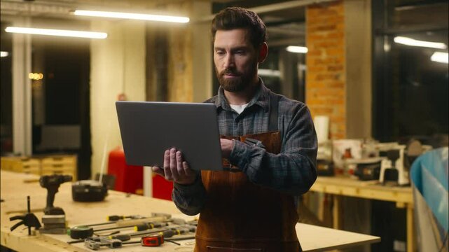 Cheerful Caucasian man wood master hold credit card typing laptop in workshop male client carpenter builder entering security number guy workman paying finance shop online craftsman Internet banking