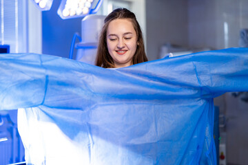Getting ready for a procedure. A young woman smiles while putting on a blue medical gown in a...