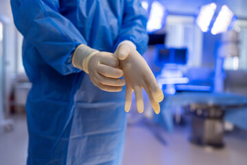 Surgeon readies for surgery. A medical professional dons gloves in a sterile operating room,...
