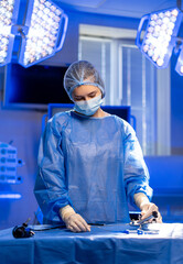 Surgeon readies tools for surgery. A medical professional in blue scrubs focuses on surgical...