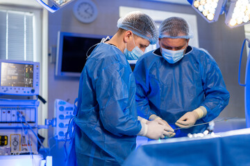 Surgery team in OR. Two surgeons in blue scrubs focus on an operation while wearing masks and...