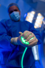 Surgeon readies glowing tool. A medical professional in blue scrubs uses a glowing instrument in a...