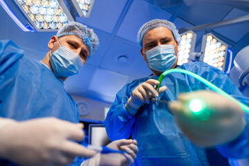 Surgeons in the OR. Two surgeons in blue scrubs are focused on a delicate operation, using medical...