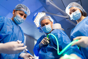 Surgery team at work. A surgical team in blue scrubs and masks works on a patient in a bright...