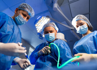 Surgeons operate in OR. Surgeons in blue scrubs and masks concentrate on a procedure, ensuring...