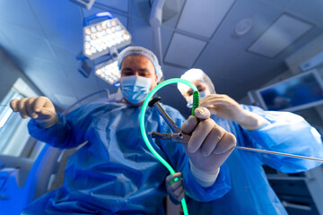 Team doing advanced surgery. Two medical professionals in scrubs work together with surgical instruments in a well-equipped operating room.