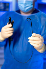 Surgeon with medical tools. Medical professional in scrub attire prepares surgical instrument in a...