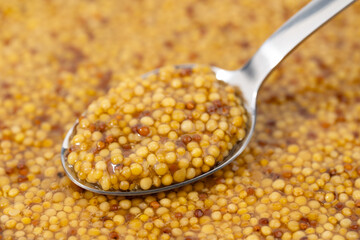 French Dijon mustard in a metal spoon, top view on mustard grains background. Gastronomy concept,...