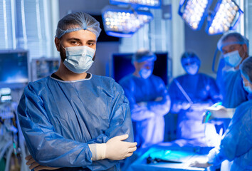 Surgical team prepares for operation. A male surgeon stands confidently in an operating room as his...