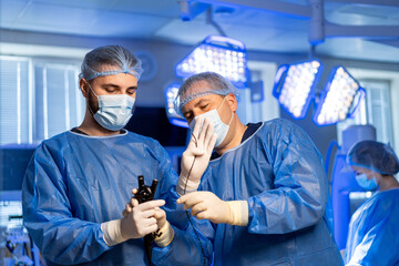 Surgeons work together. Two surgeons in blue scrubs examine a medical instrument in a well-lit...