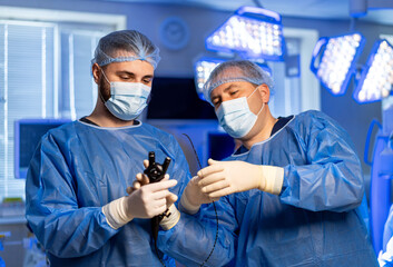 Surgeons readying for surgery. Two surgeons in blue scrubs and masks collaborate in a bright...