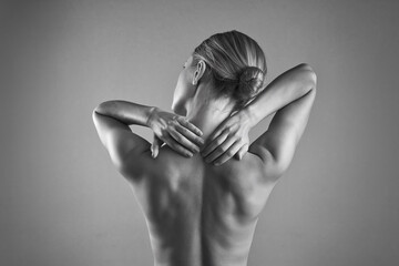 Black and white photo of woman's back, hands massaging neck and shoulders, showcasing muscle tension or relaxation, suggesting wellness, therapy or healthcare