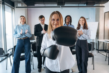 Woman is in boxing gloves. Group of young business people are in conference room