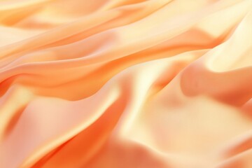 Fototapeta premium Smooth peachy-orange fabric draped in soft, flowing waves. Close-up view showcasing luxurious texture