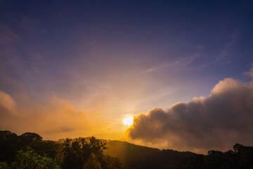 stunning mountainous landscape at sunrise with vibrant orange and pink hues illuminating the clouds against a blue sky. layer of mist settled in the valley, giving the scene a dreamy.