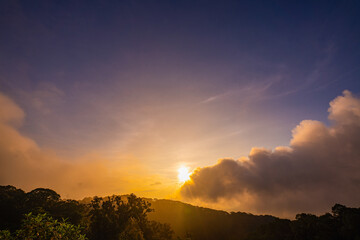 stunning mountainous landscape at sunrise with vibrant orange and pink hues illuminating the clouds against a blue sky. layer of mist settled in the valley, giving the scene a dreamy.