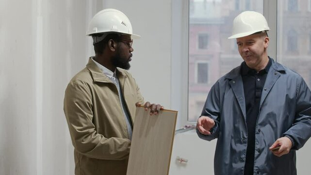 Medium shot of two male bicultural interior designers examining color samples on wooden plank working on construction site