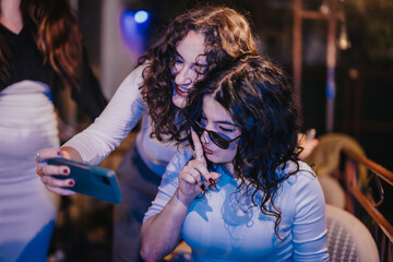 Fototapeta premium Two smiling friends take a selfie together during a festive party, capturing fun moments in a cozy setting while enjoying a relaxing and cheerful evening.