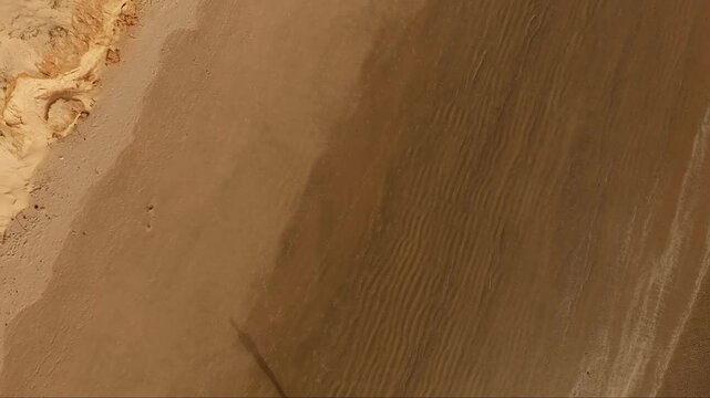 Vue a&eacute;rienne verticale d&rsquo;une plage d&eacute;serte du S&eacute;n&eacute;gal avec contraste graphique entre sable sec et humide, plan en &eacute;l&eacute;vation progressive, textures naturelles en bord d&rsquo;oc&eacute;an