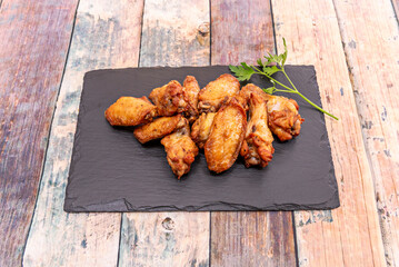 Fried chicken wings on a black slate tray on a wooden table
