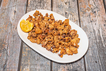 A wonderful tapa of Andalusian-style fried squid with a slice of lemon on a white porcelain tray